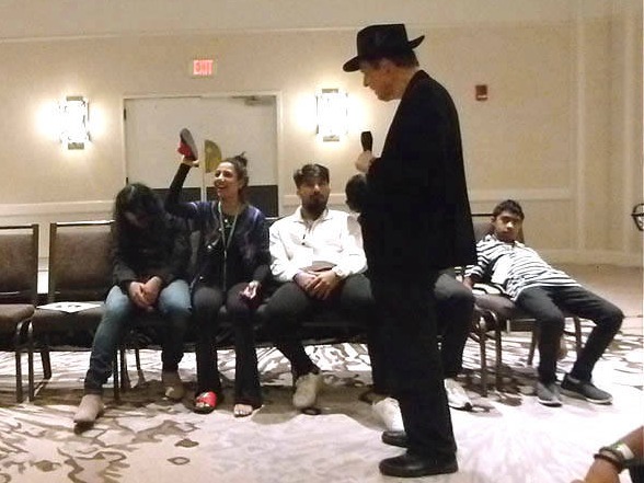 Woman holds her shoe in front of er face at Chicago area association hypnosis show.