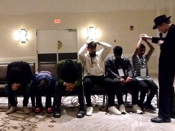Row of seated volunteers slumped over or with their arms over their heads at a Chicago area association hypnosis show. 