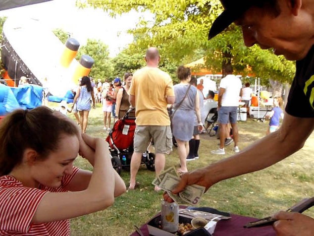 Girl with hands stuck on her head offered money by Hypnotist Mister Vibe at a Chicago park festival.