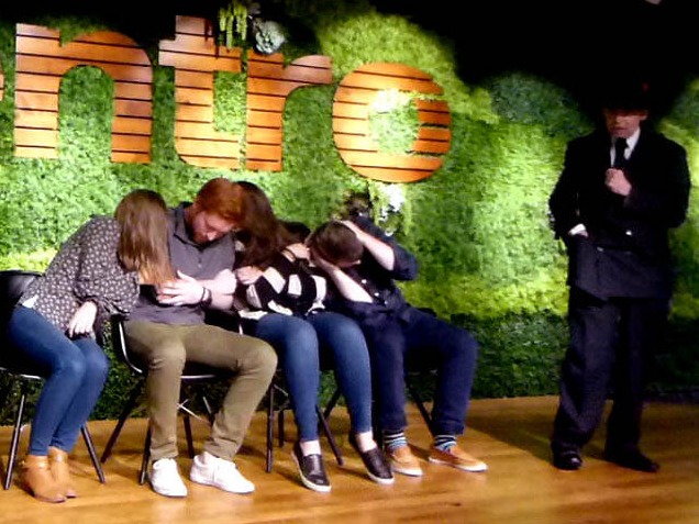 Seated row of volunteers huddles together at a Chicago area office party hypnosis show.