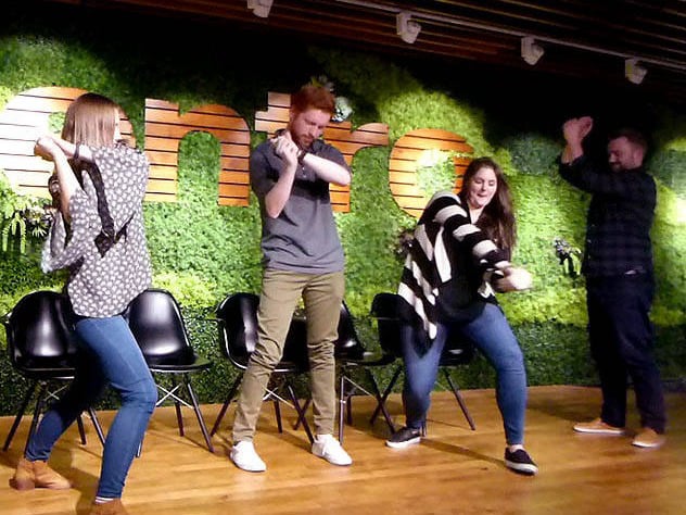 Standing volunteers wave their arms around at a Chicago area office party hypnosis show.