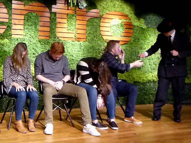 Hypnotist Mister Vibe gives seated volunteer a bandage at a Chicago area office party hypnosis show.