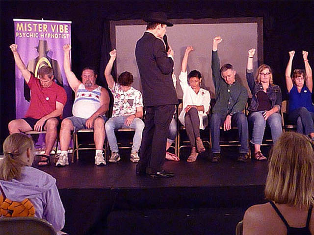 Row of people on stage at a hypnosis show raising their hands