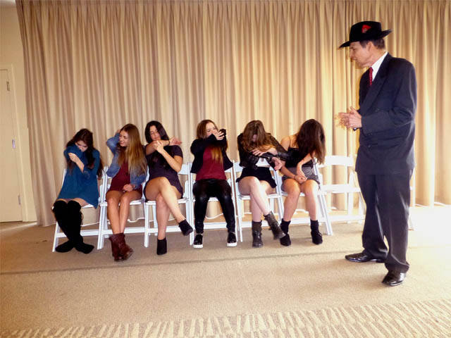Row of seated girls smelling their elbows at a Chicago area Sweet 16 party hypnosis show..